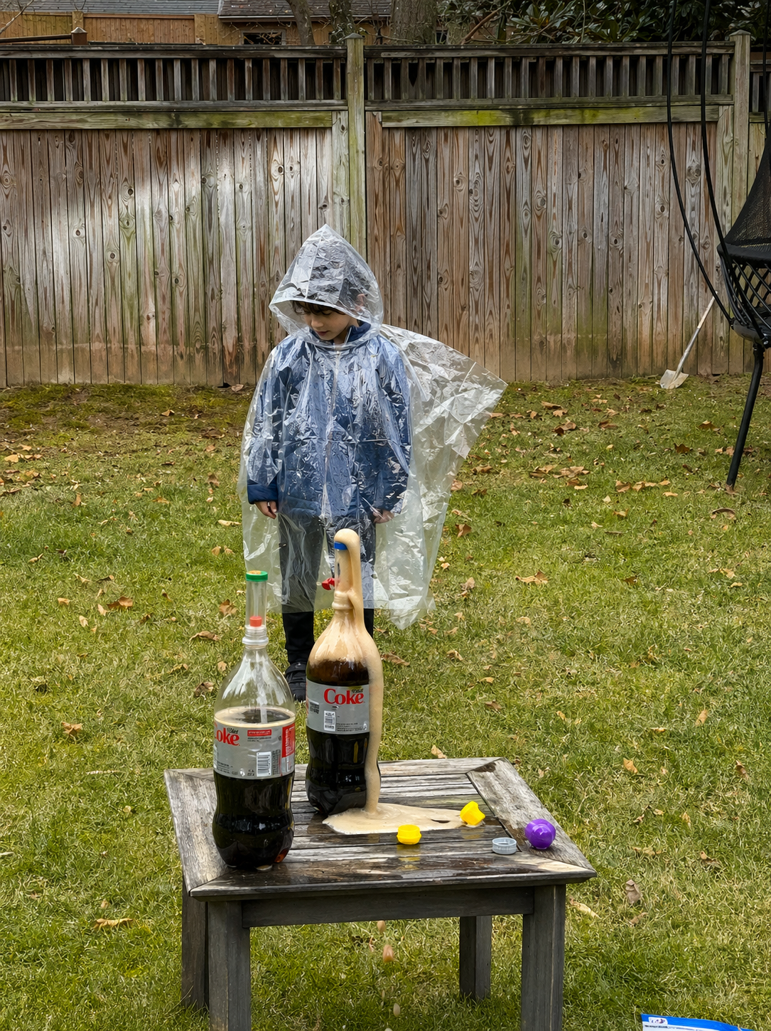Child in rain poncho doing an outdoor science experiment with soda bottles in the backyard